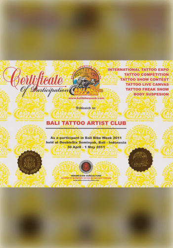 A shimmering, gold-embossed certificate hanging on a bamboo wall, honoring a tattoo artist of East Asian descent as the recipient of the "Golden Needle Award" for their exceptional precision and creativity in Bali's tattoo scene.